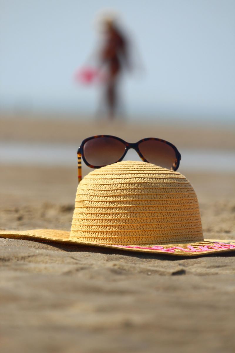 A straw hat and sunglasses resting on the sand