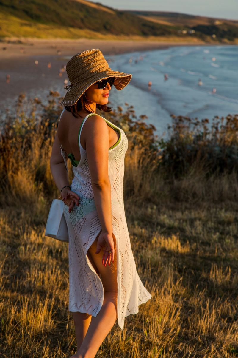 Woman in a white crochet dress and straw hat on a grassy coastal cliff