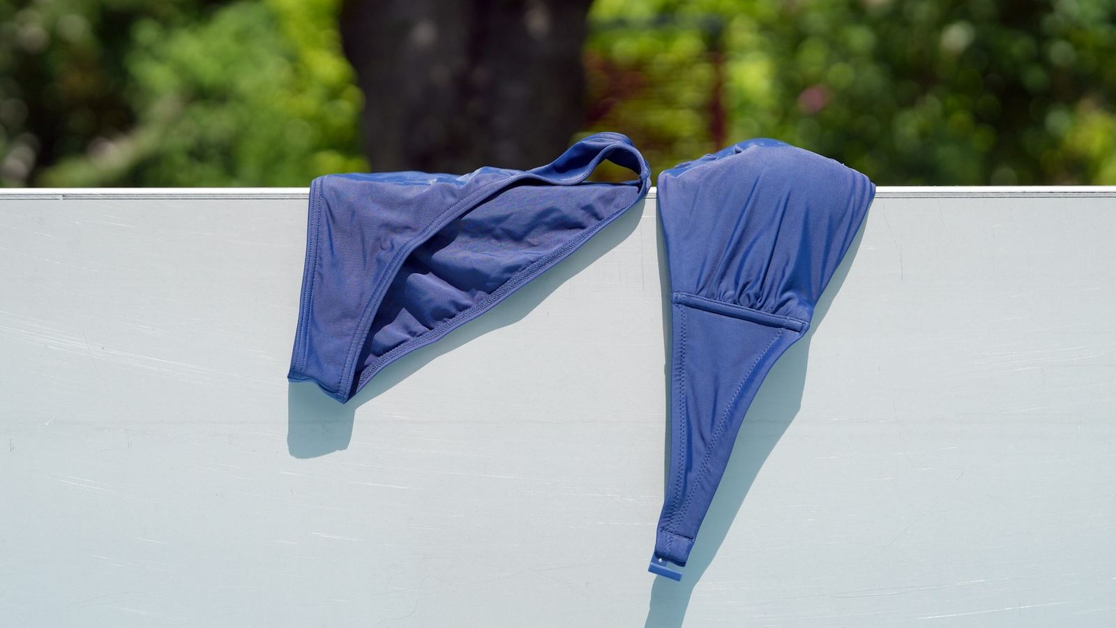 A blue bikini drying over a white wall in the sun